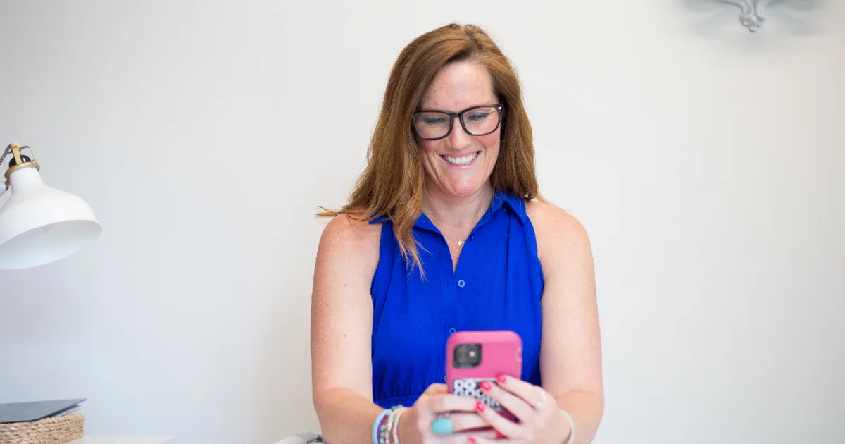 Mujer sonriente en su escritorio respondiendo mensajes en su celular