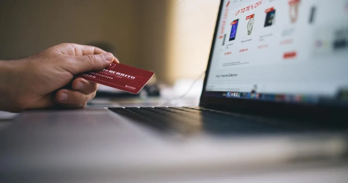 Persona con una tarjeta de crédito en la mano comprando en una tienda online desde su laptop