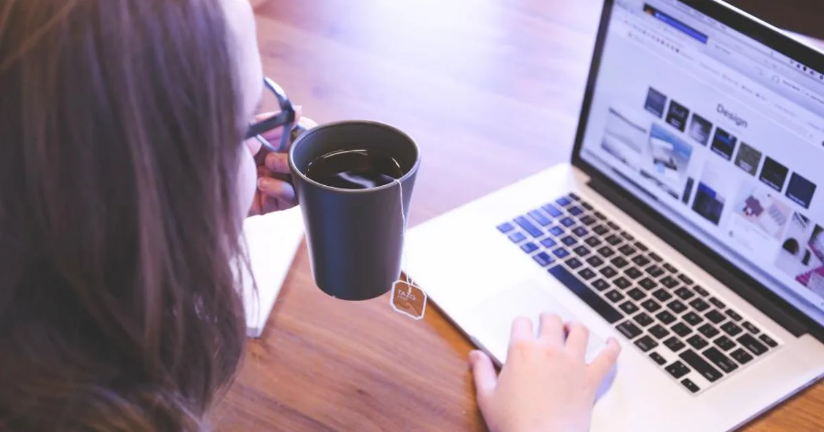 Mujer revisando un sitio web en su laptop mientras toma café