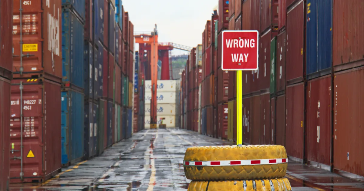 Señal de tránsito que dice Wrong Way (camino equivocado) entre contenedores de carga
