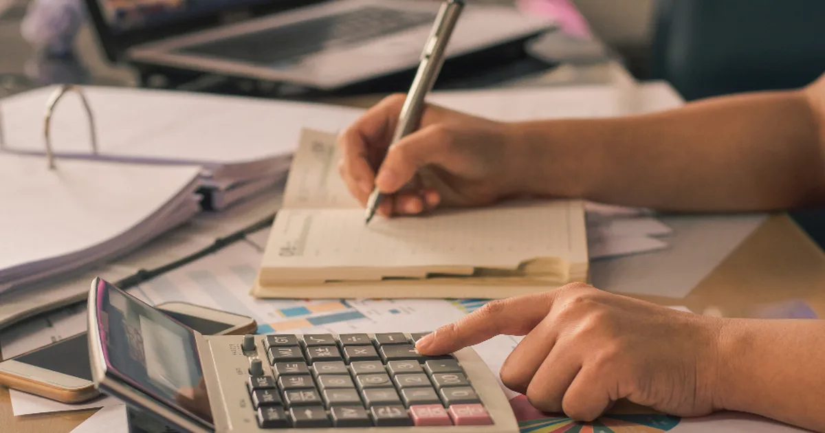 Manos de una persona usando una calculadora y tomando notas junto a documentos contables