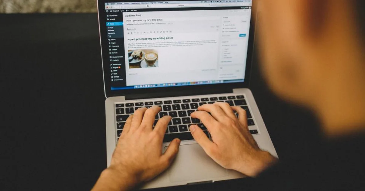 Manos escribiendo en una laptop con el editor de WordPress abierto en pantalla